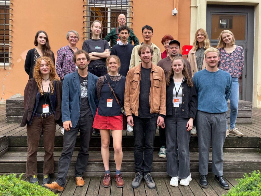 A group of early to mid career journalists posing for a photo on the steps of a small building. They are the Climate Arena Fellows from 2024.