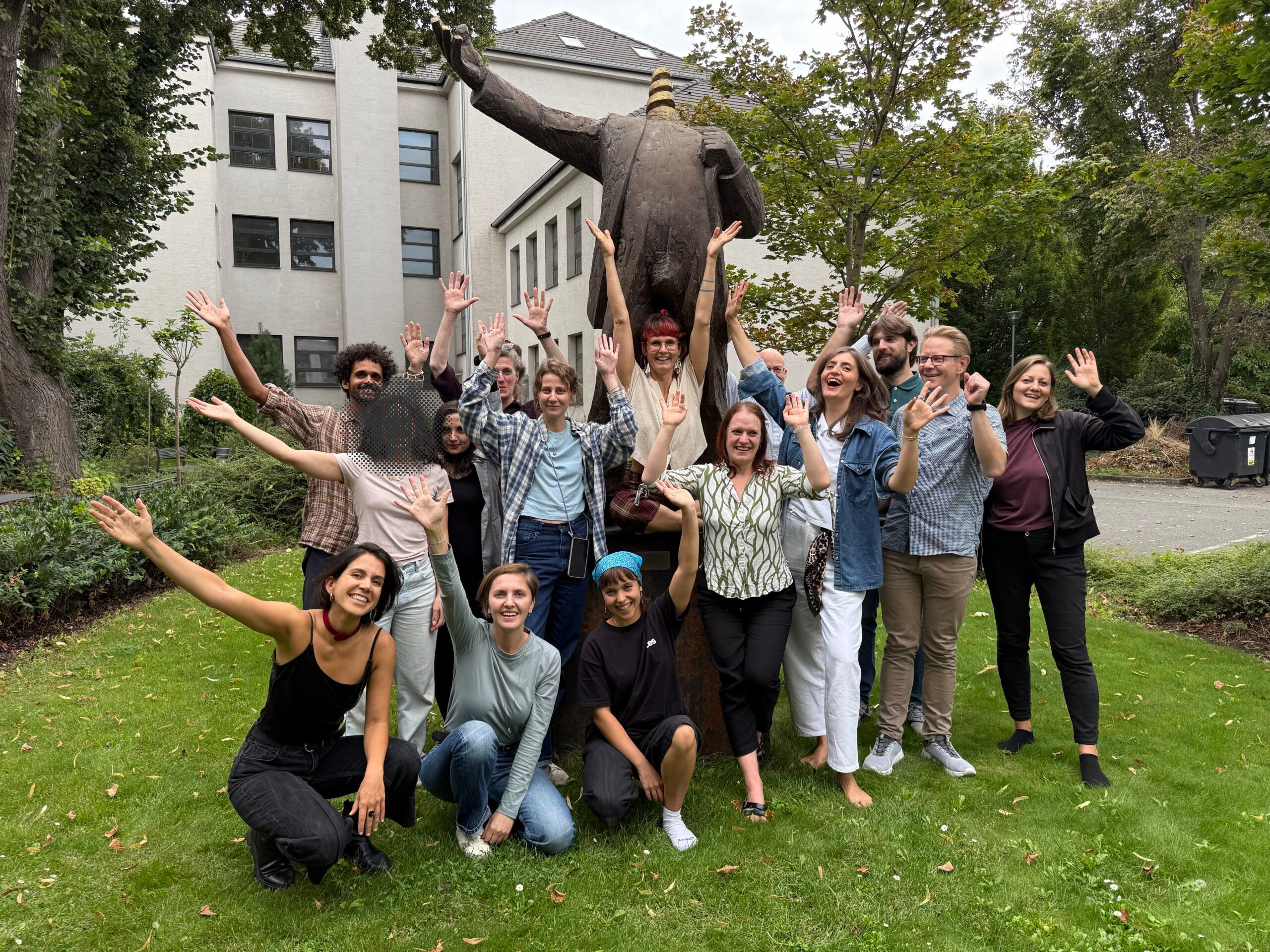 The 2025 Climate Arena fellows stand with arms outstretched in front of a statue in Bratislava. (One participant's face is redacted at their request.)