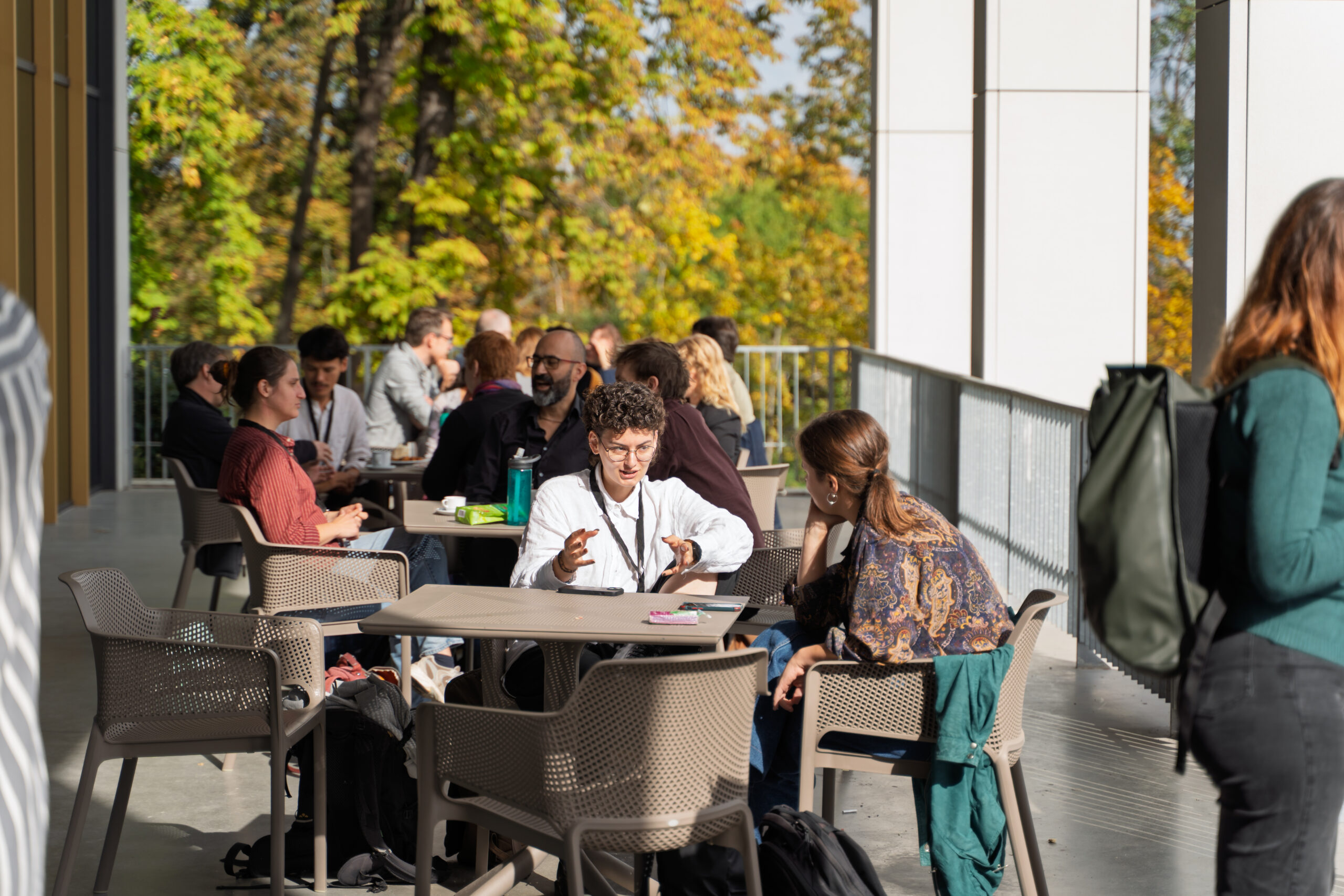 A terrace populated with journalists at tables, in discussion. In the foreground, a couple of young journalists wearing Climate Arena lanyards are discussing animatedly.